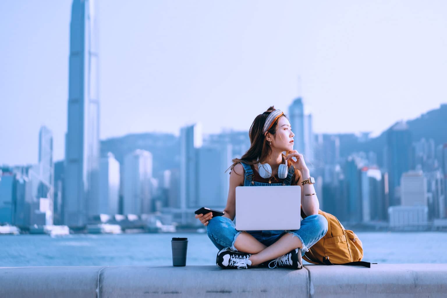 Woman sits on on rooftop with headphones and a laptop